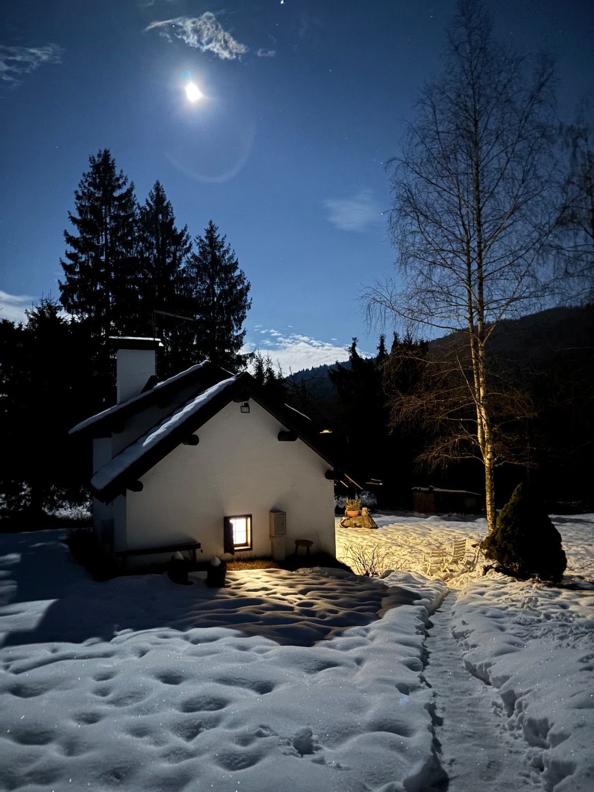 La baita di notte sotto la luna, con il sentiero tracciato nella neve